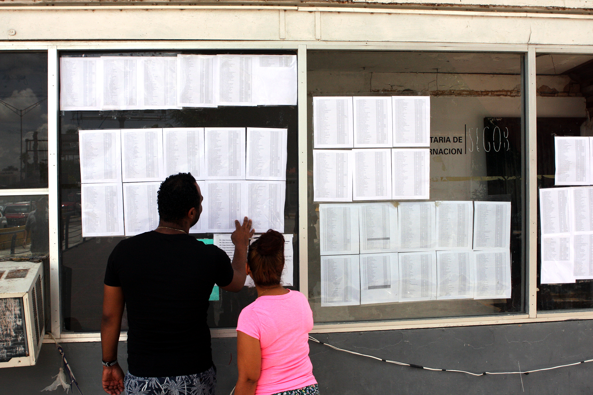 Photo of people waiting to cross international bridge looking for their names on a list.