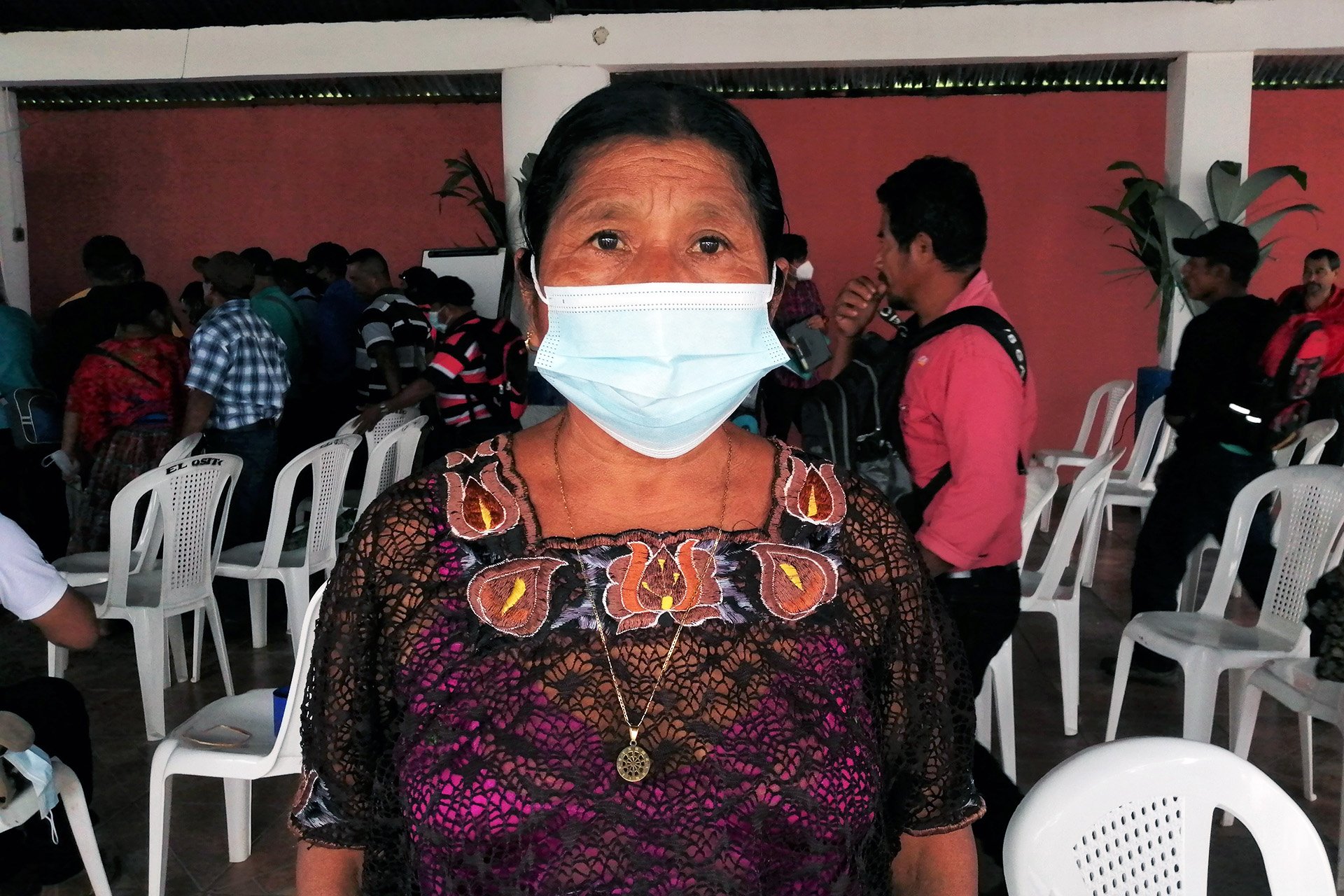 A woman stands facing the camera wearing a face mask. 