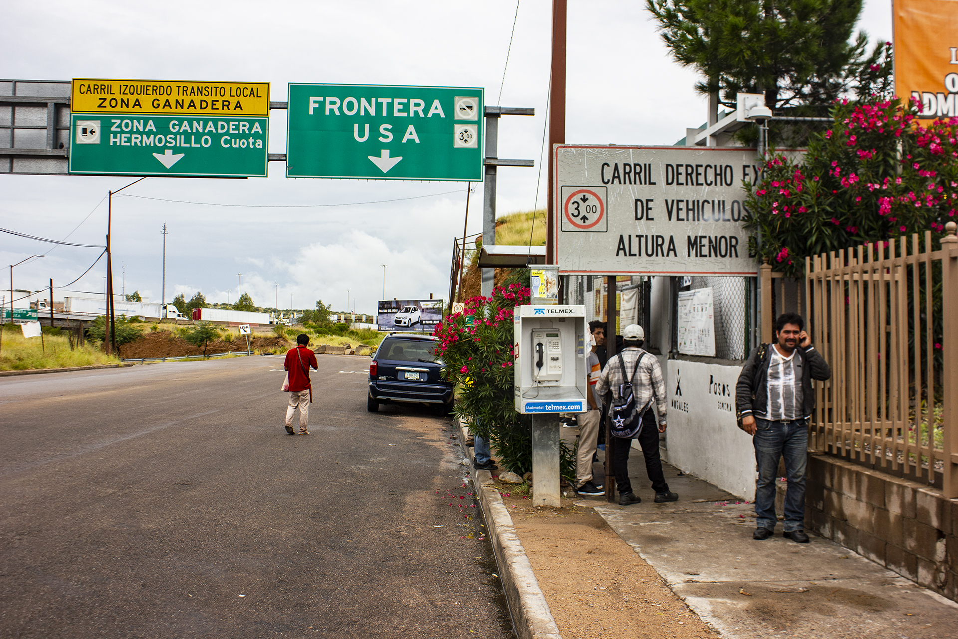 People on a street with a highway sign pointing to the border.