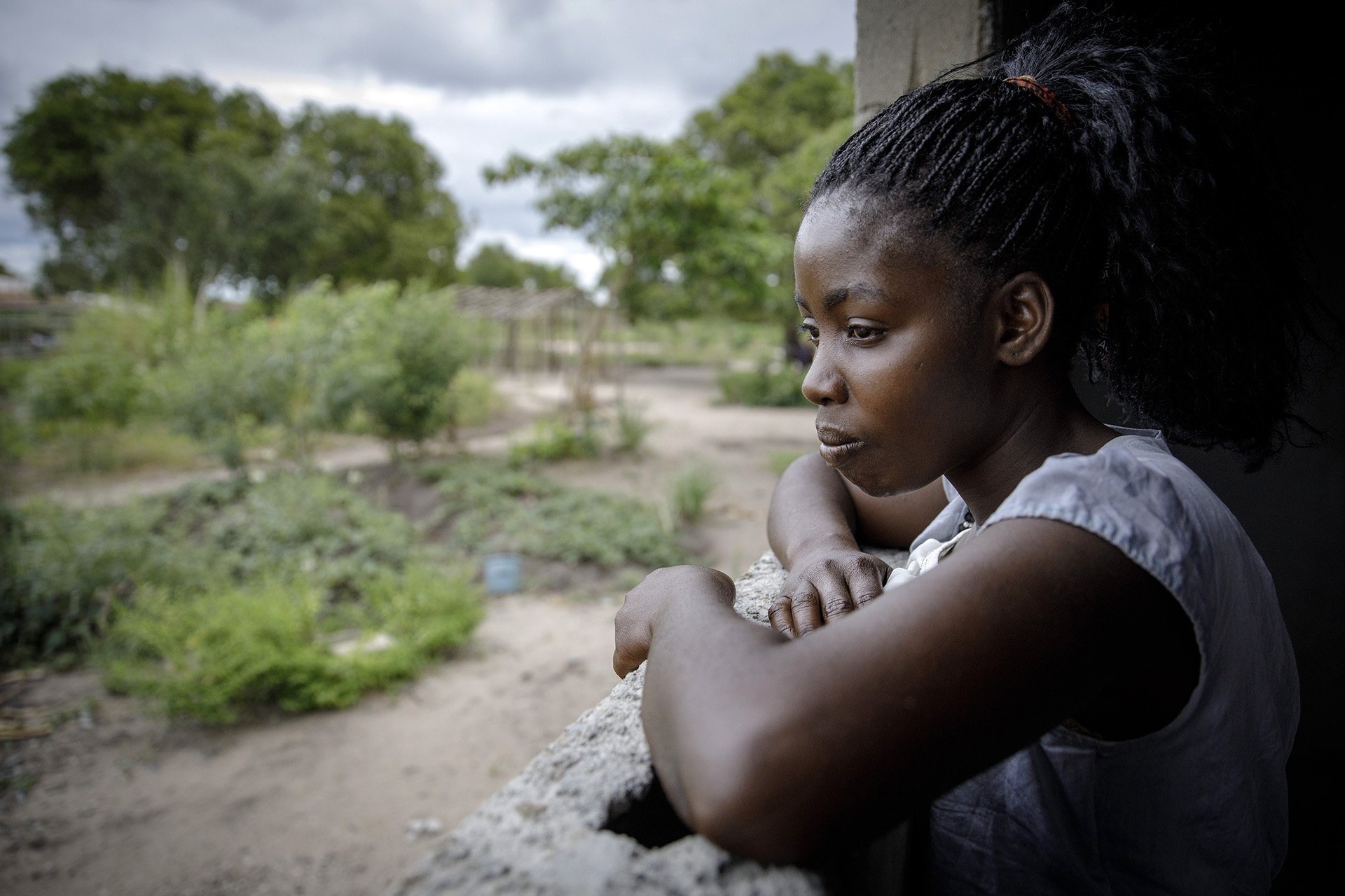 A woman leans on a balcony looking out onto a field. 