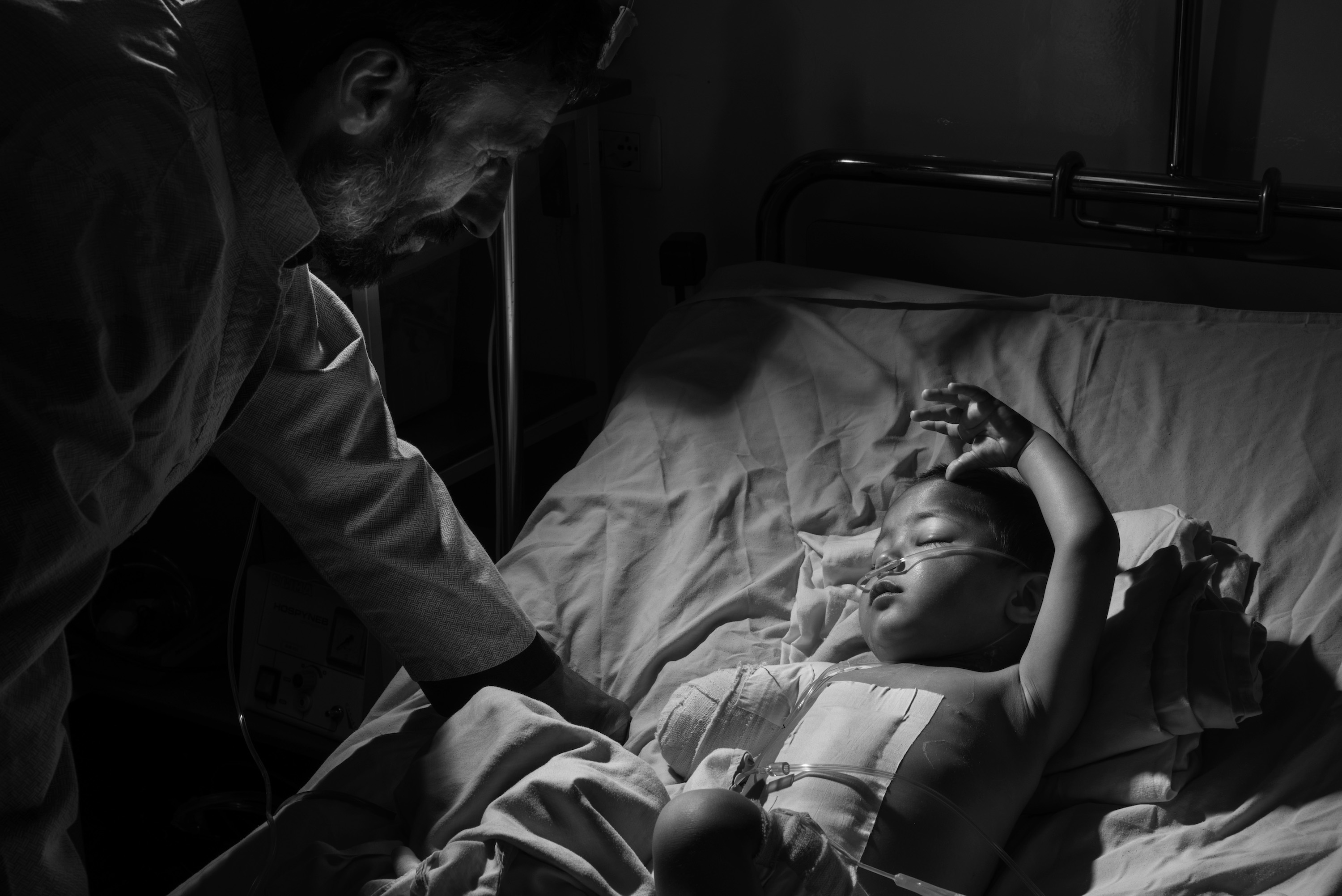 A child in a hospital bed with father looking over