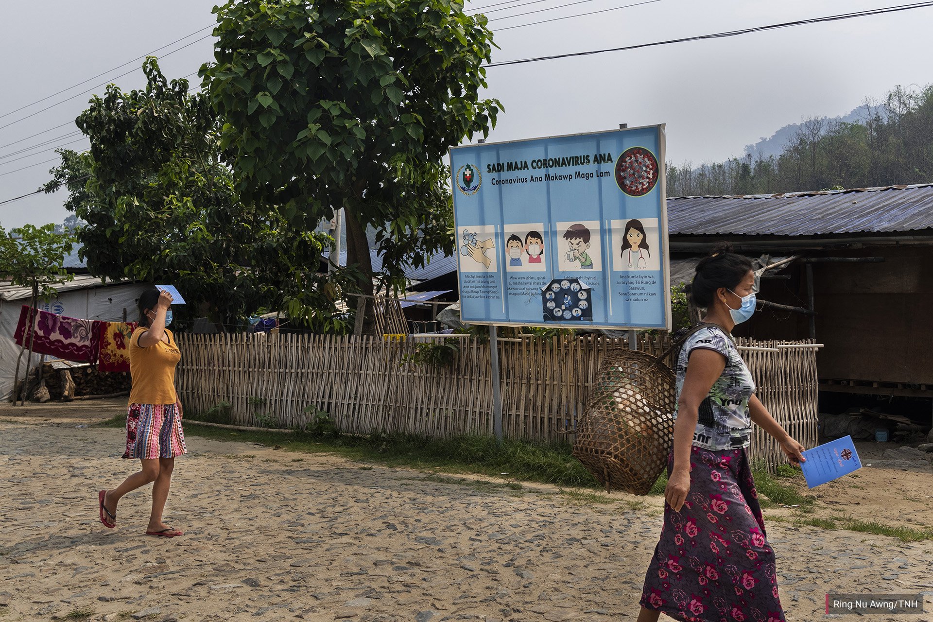 Women walk past a vinyl banner in Jinghpaw