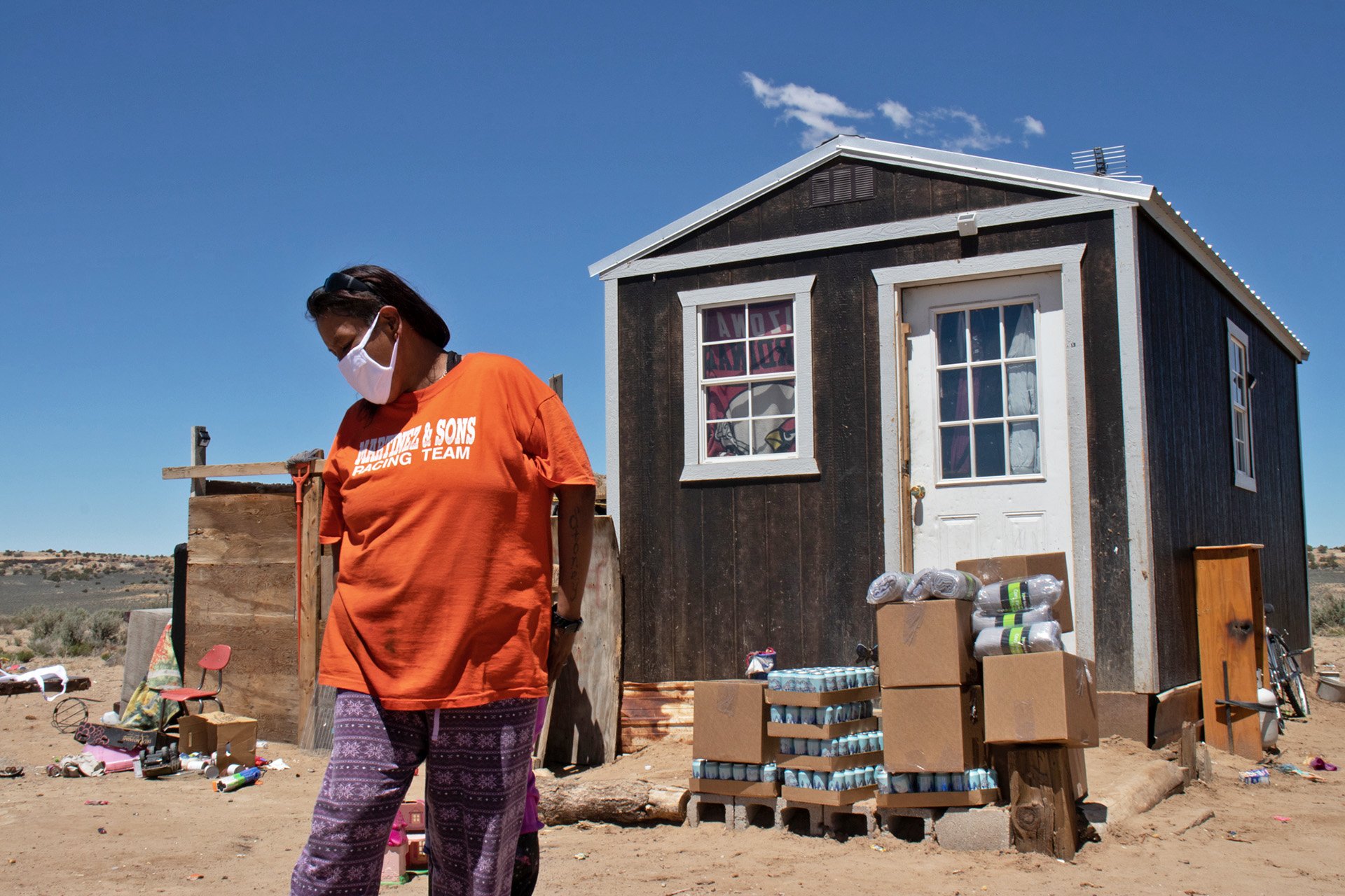 Velma Pinto stands in front of the house where she lives with her husband and five children. The family have no running water. Here, they have just received a delivery of water from Indigenous Lifeways.