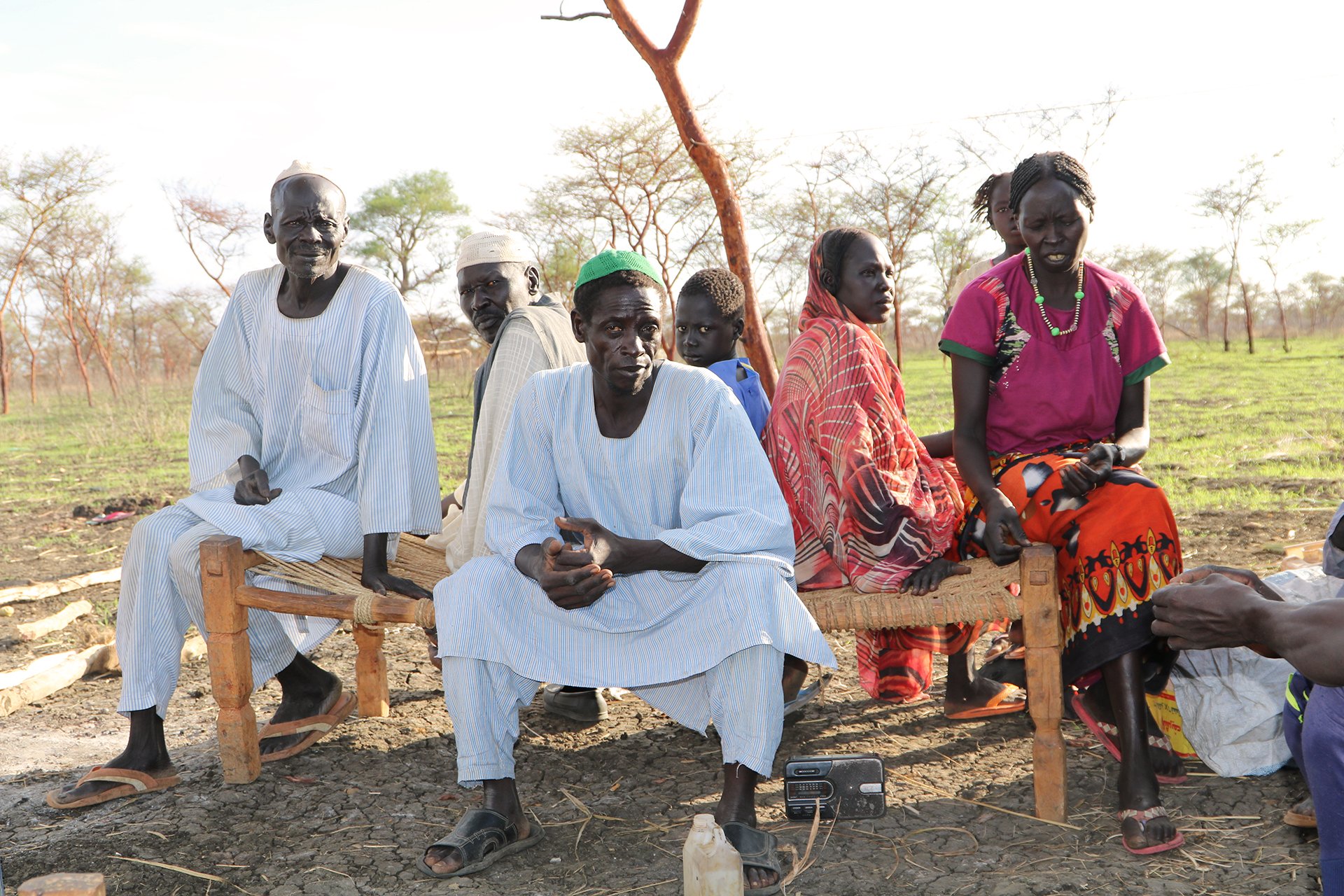 Noor Faki sits on a bed in his yard with his neighbours in South Ulu village in Blue Nile state.