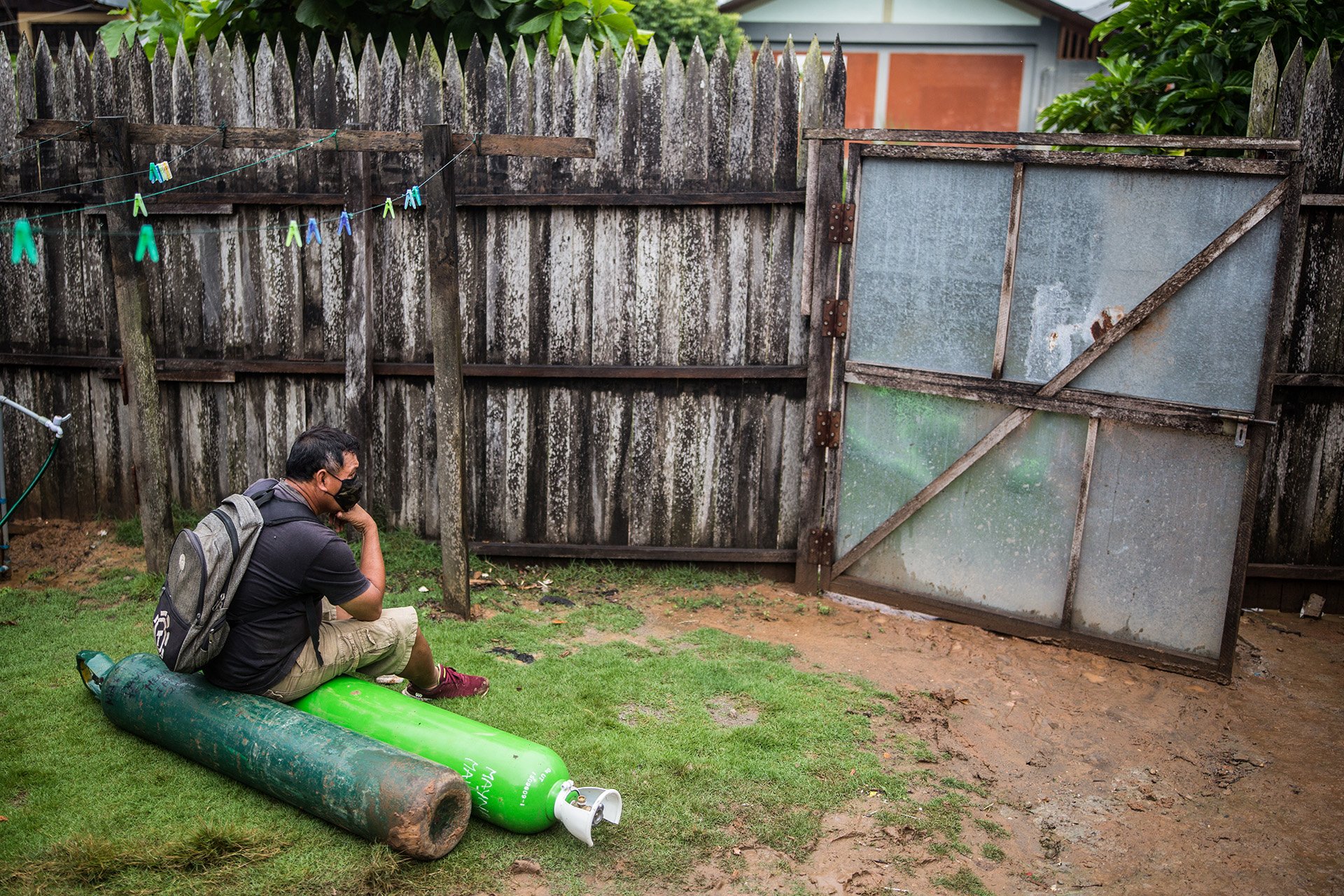 A man sits on two green oxygen tanks in a grassy yard. 