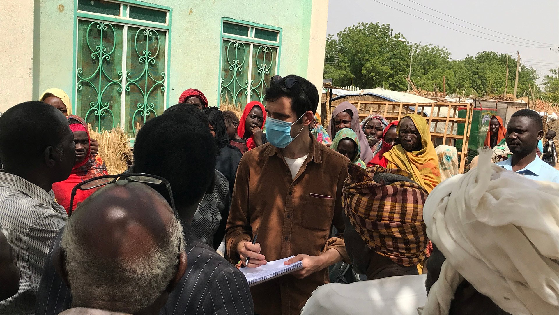 A reporter speaks to a group of people outside a small building.