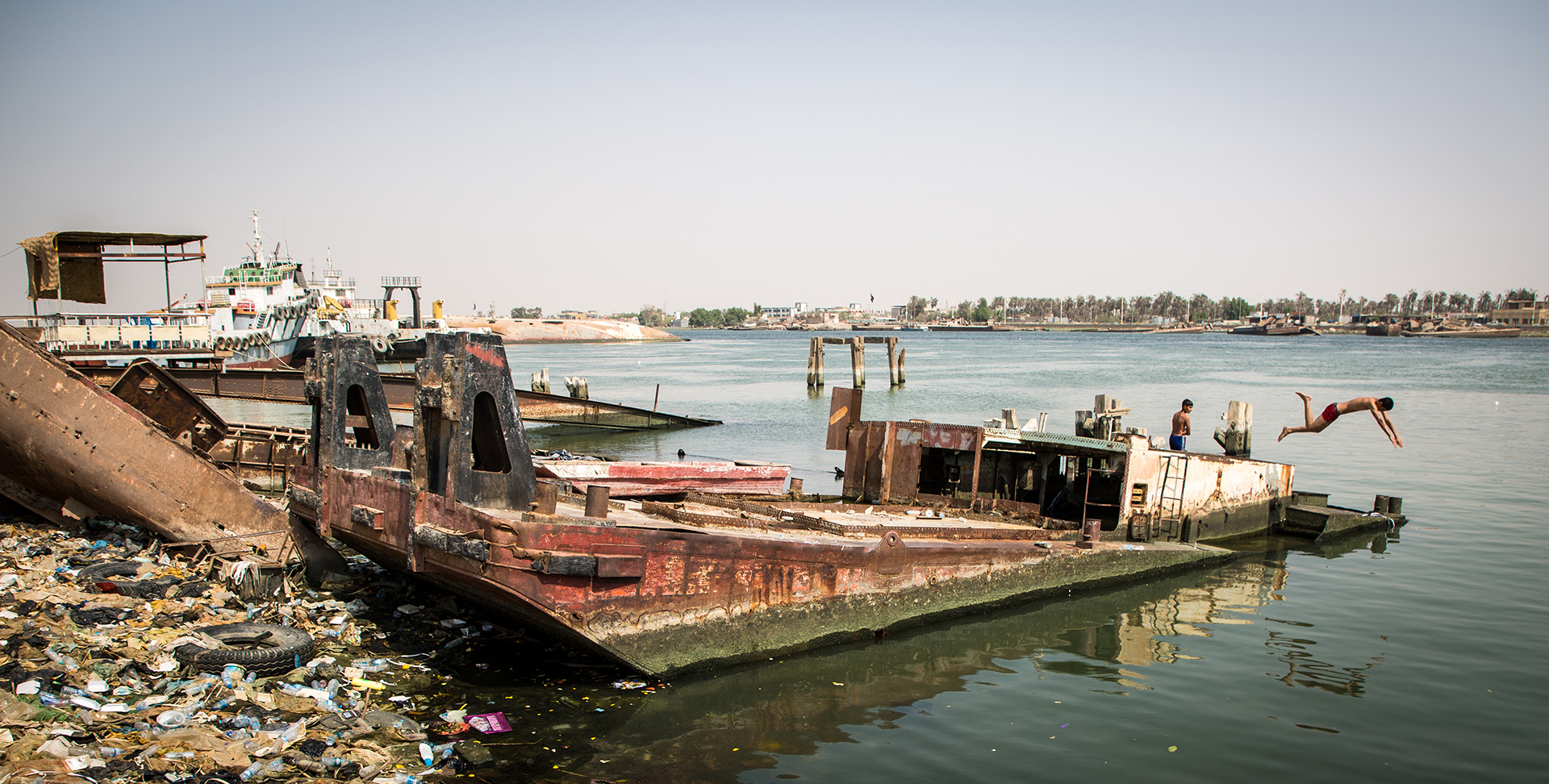 Young man diving from a wrecked ship into the polluted Shatt al Arab river in Basra.