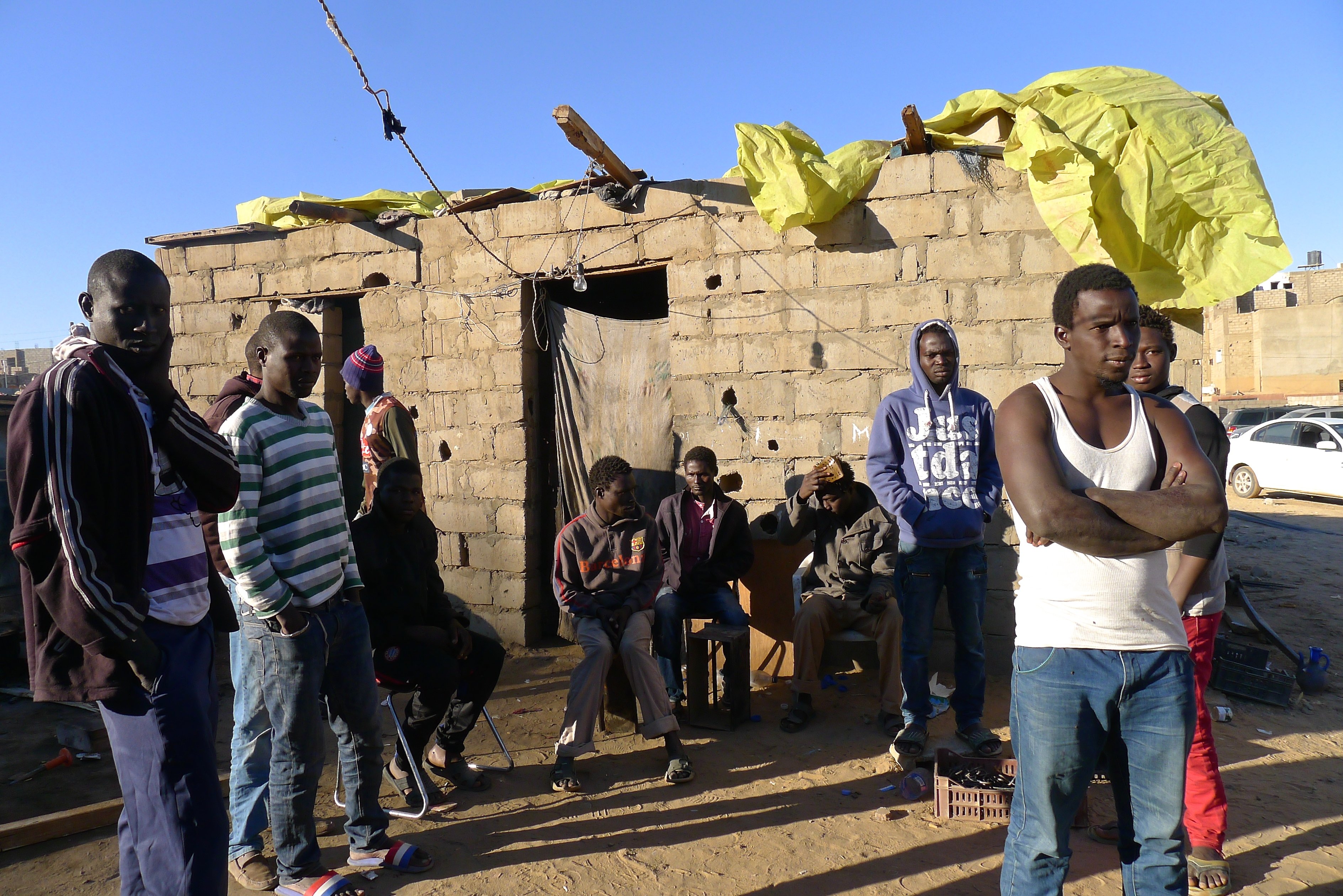 A group of men standing around a small concrete building A group of men