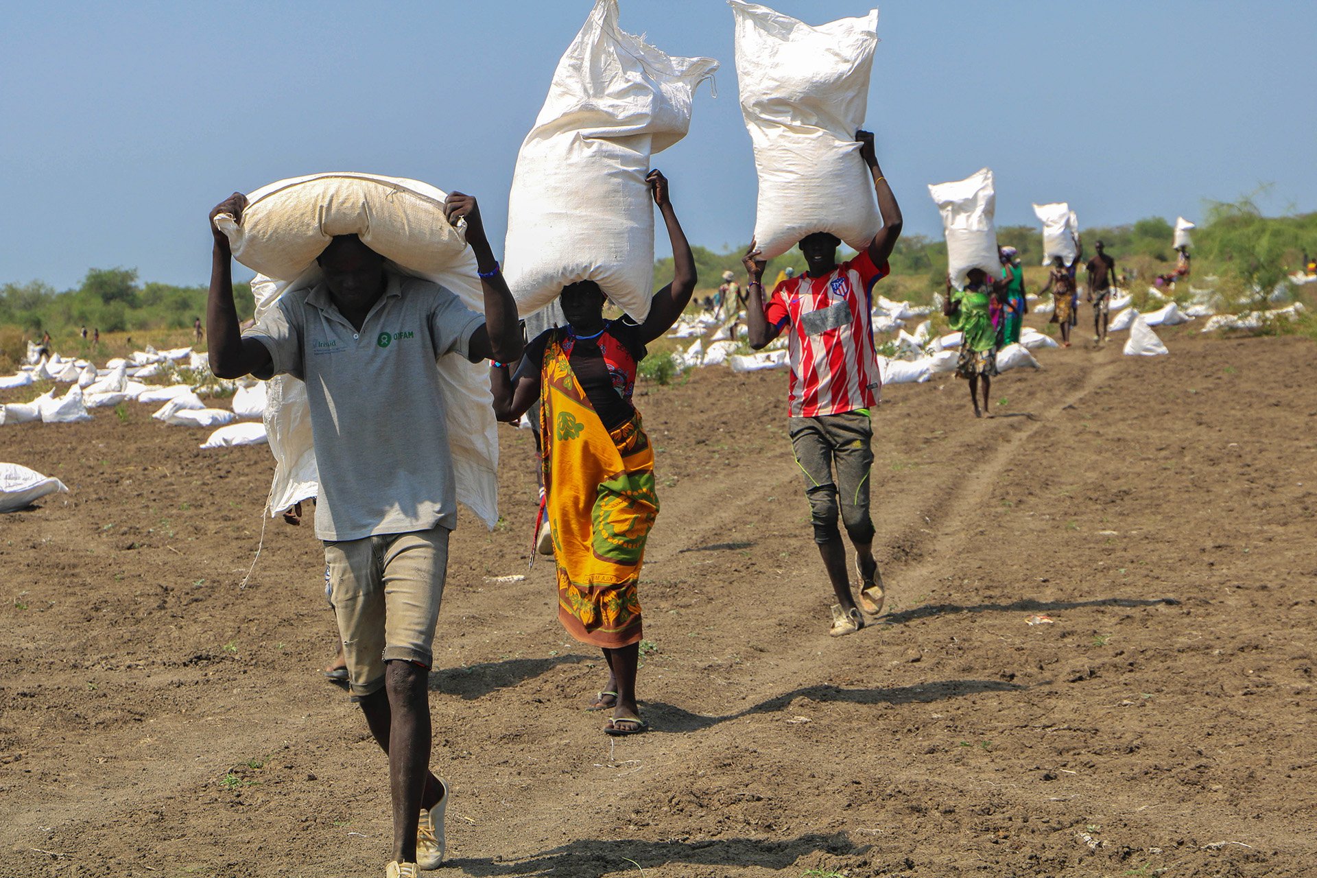 Three residents carry food aid bags on their shoulders as they walk towards the camera