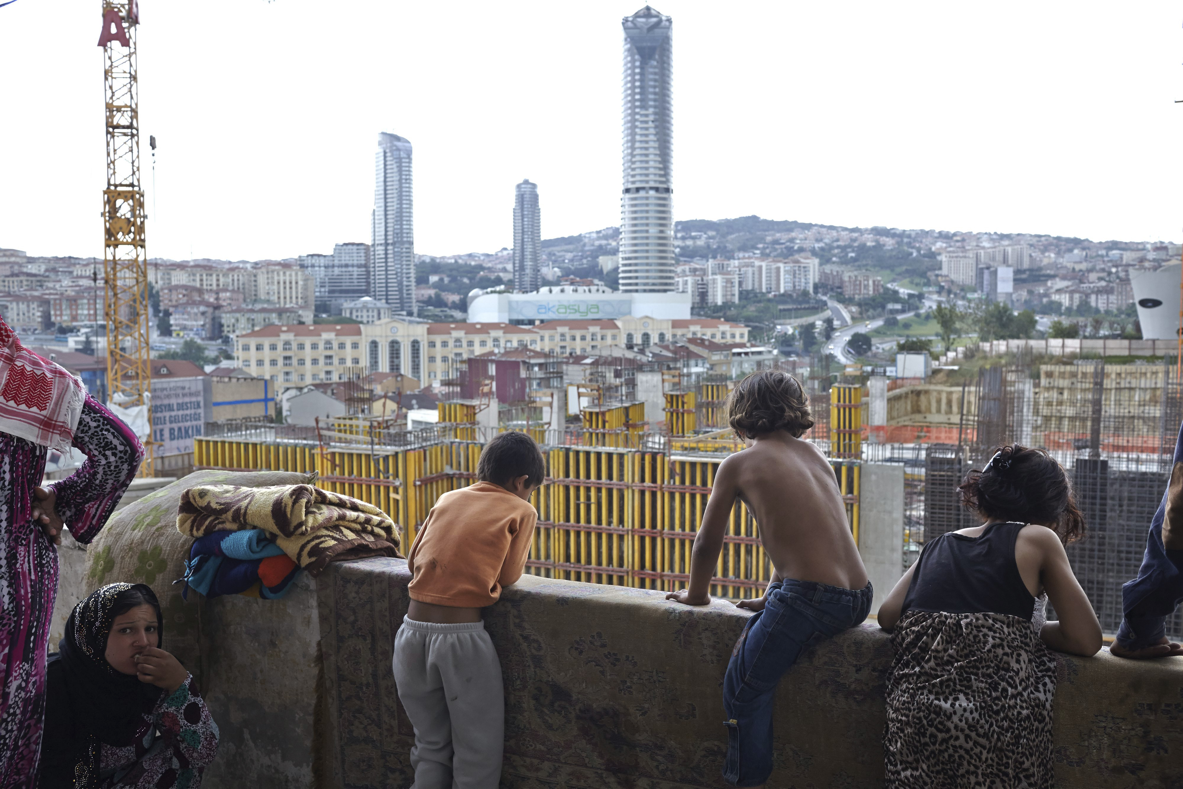 Children look out from the balcony of a tall building onto new construction in Istanbul