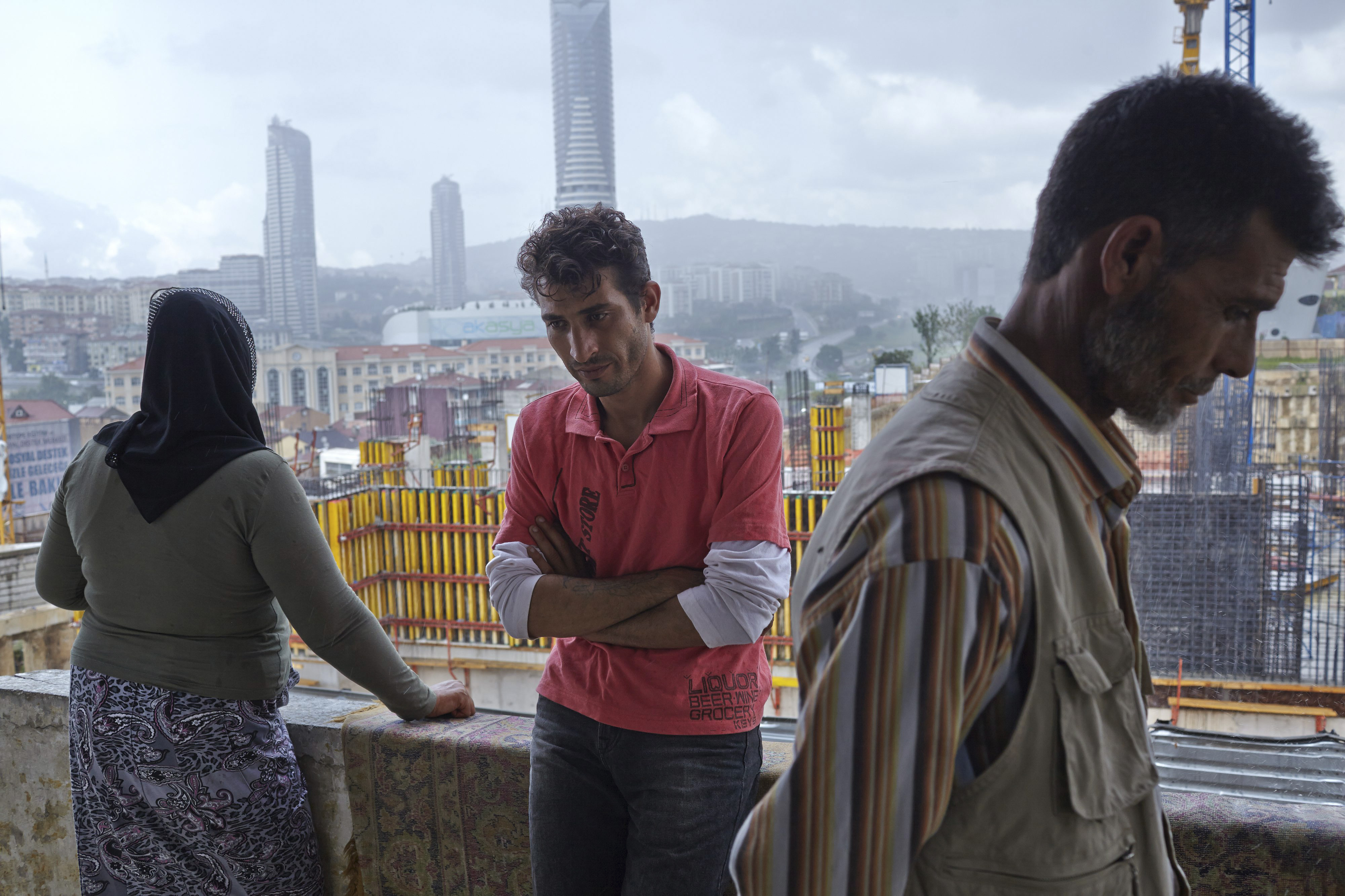 Three people look off camera on a balcony in Istanbul above new construction