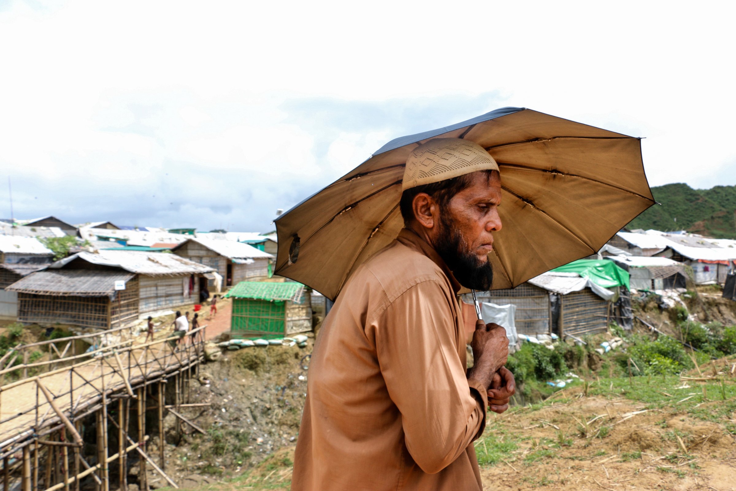 Photo of a man walking in a Rohingya camp with an umbrella in Bangladesh