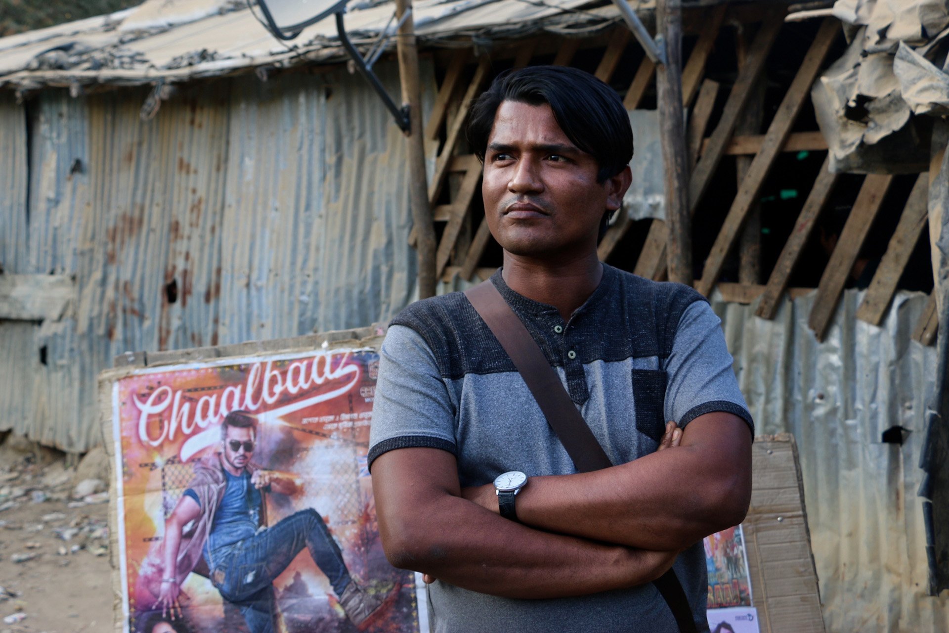 A man with his arms crossed in front of a movie poster