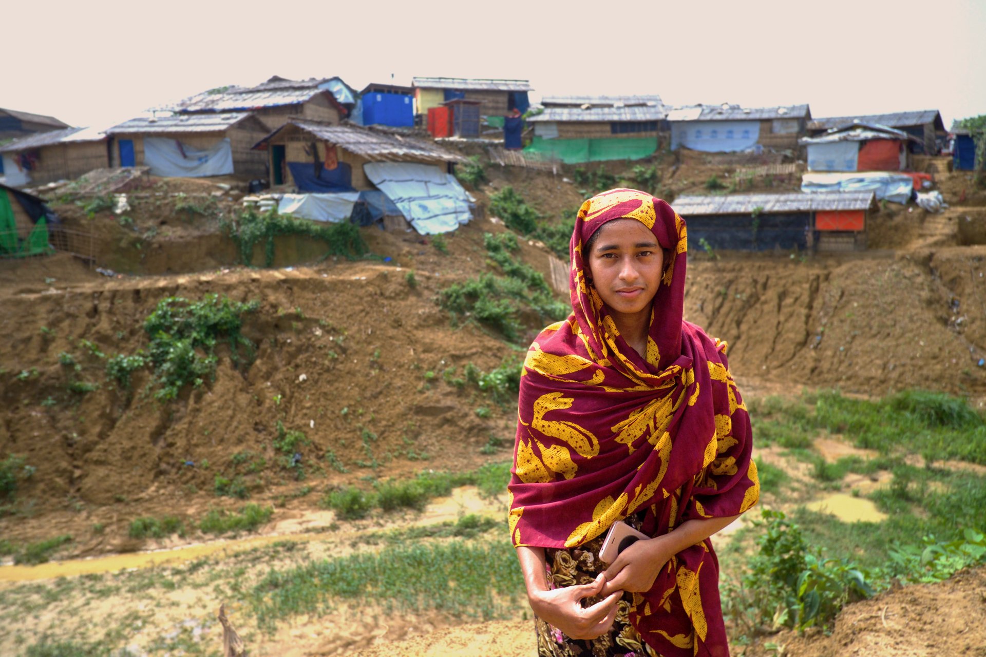 A woman looks at the camera in front of a refugee camp in Bangladesh