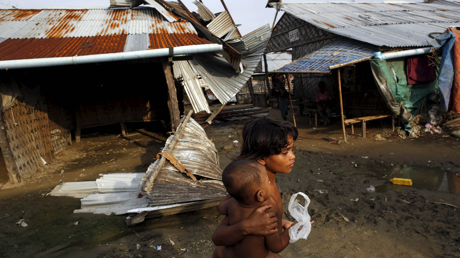 Rohingya girls pass in front of a damaged shelter in a displacement camp outside Sittwe in Myanmar’s Rakhine State in August 2015.