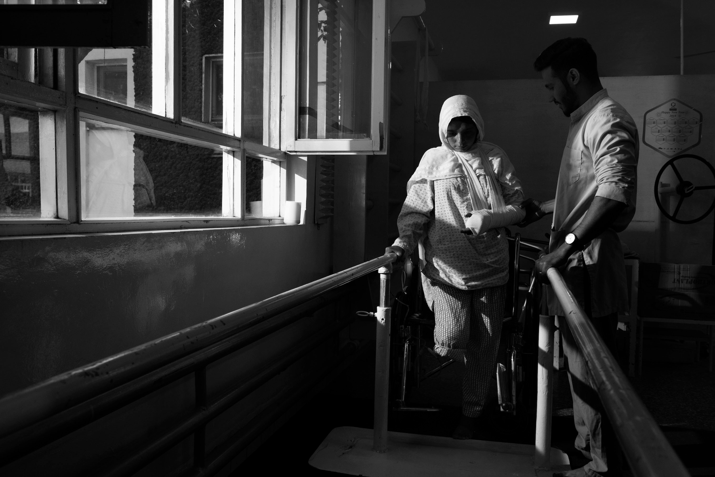 A woman walks with help of railings and medical staff