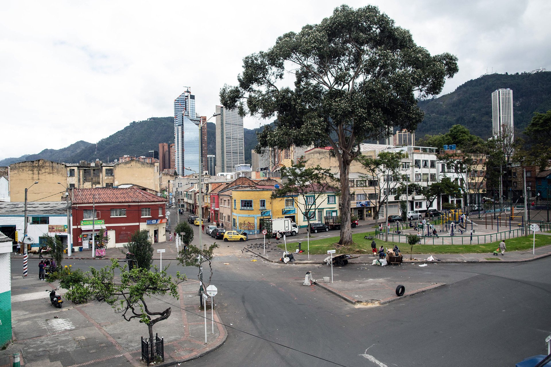 A upwards angle view of an traffic intersection with buildings and a small mountain with vegetation on it in the background.