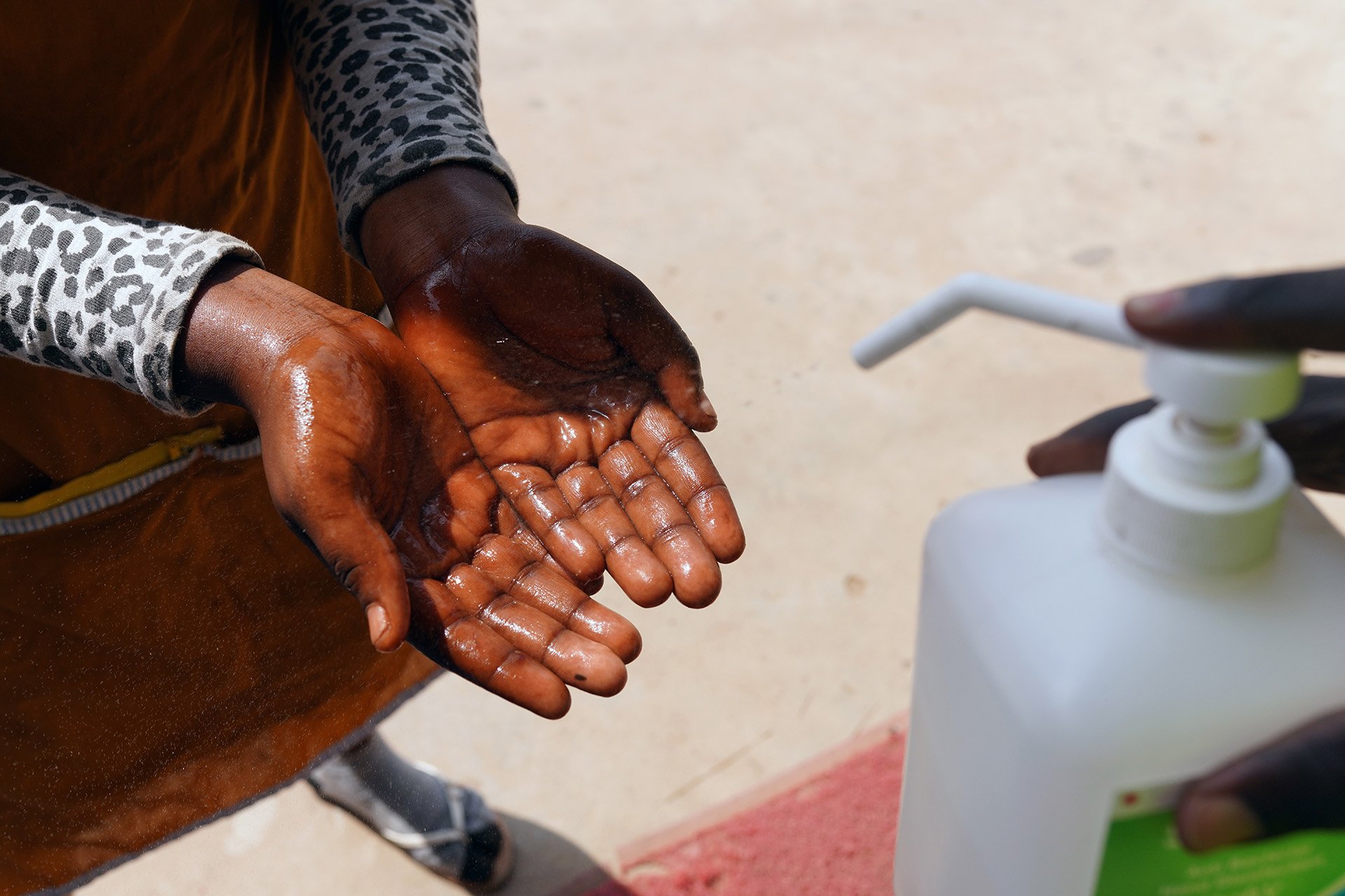 A pair of hands with the palms facing up are held out and a bottle of hand sanitizer is sprayed onto them