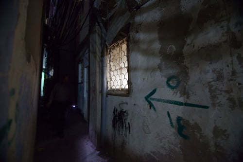 A dark corridor where a barely visible man uses a keyring light to help navigate in Beirut, Lebanon.