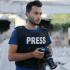 Moawia Atrash in a press vest with a DSLR camera in hand.