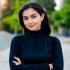 This is a headshot of aid worker and journalist, Tiara Itaii. She's wearing a dark blue turtleneck. Her arms are crossed in front of her. Her hair is dark and her head is slightly tilted to the right and she is smiling but not showing her teeth.