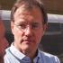 A closeup of David Carden looking slightly towards his right at a person who is off camera. He is wearing a light blue button up shirt and glasses. 