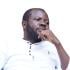 Nicholas Bahati Ndoolé is pictured leaning back, with his left hand raised to his chin and his face tilted towards his left shoulder. His eyes look over his shoulder.
