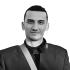 This is a headshot of Mohammed Mhawish. He is pictured smiling without showing his teeth. He wears a dark jacket, 