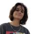 Rita Baroud is pictured looking down and smiling at the camera. The shot is placed at a low angle. She wears a grey graphic t-shirt and a silver chain.