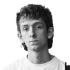 A headshot of Euan Wallace. He looks at the camera without smiling. He wears a white t-shirt.