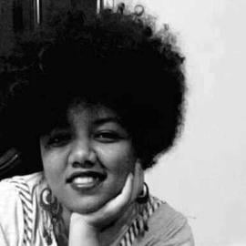 This is a headshot of Rawh Nasir. She is a part of the Gereif West emergency room volunteers group. Her headshot is in black and white. She is smiling at the camera, resting her face on her left hand.