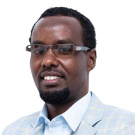 This is a headshot of Mohamed Yarrow. He is pictured smiling at the camera. He wears glasses and a light blue checkered blazer and shirt.