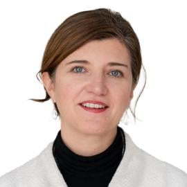 This is a headshot of Jessica Bither. She wears a black turtleneck and white coat. She smiles at the camera.