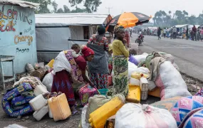 A group of displaced people in Goma stand next to a road with their belongings. 
