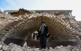 Badr el-Din Mouhanna stands under a brick arch of a building that has been turned into rubble.