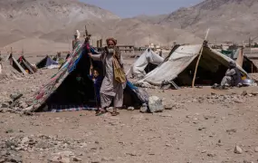 A man stands next to a tent in a makeshift camp.