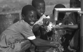 [Zambia] At a community school in Nthombimbi, Zambia, children gather around a water pump. The school is staffed and maintained by the community for children who cannot afford to attend formal school. Many of the pupils are orphans.