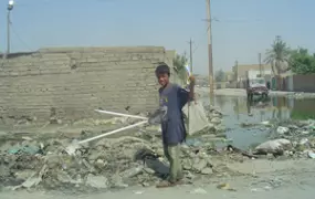 [IRAQ] A boy pulls flourescent light tubes out of the trash piled around the sewage in the street in Kamaliya, a poor suburb of Baghdad.