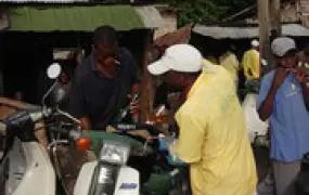 [Benin] Motorcycle taxi drivers filling their tanks with contraband petrol from Nigeria at a roadside stall in Cotonou, Benin, April 2005.