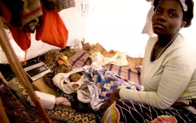 Kibati I IDP Camp: North Kivu, DRC: Furaha sits with her child inside her home in Kibati I IDP Camp, Goma, DRC. For the last two years, Furaha has shared her small house with her parents while waiting for the government declare it safe for displaced peopl