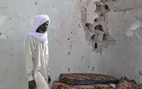 A resident of Tayuri stands against a bullet-riddled wall of his house. Part of it was destroyed during the clashes in Libya