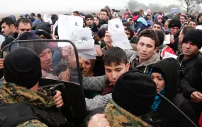 Migrants and refugees wave their Greek registration papers at the border with Macedonia where only certain nationalities were being allowed to cross.