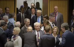 US President Trump looking isolated in a room full of people talking