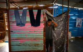 A man stands in a makeshift shelter with light pouring in from gaps in slats