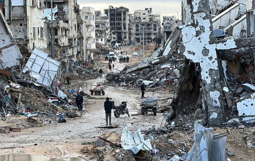 A few people are walking down a street. Destroyed buildings stand on both sides.