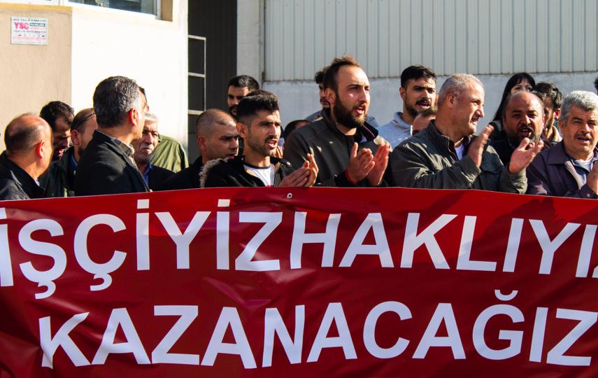 Workers at Vera Ambalaj are pictured during a strike. They are photographed mid chanting behind a banner.