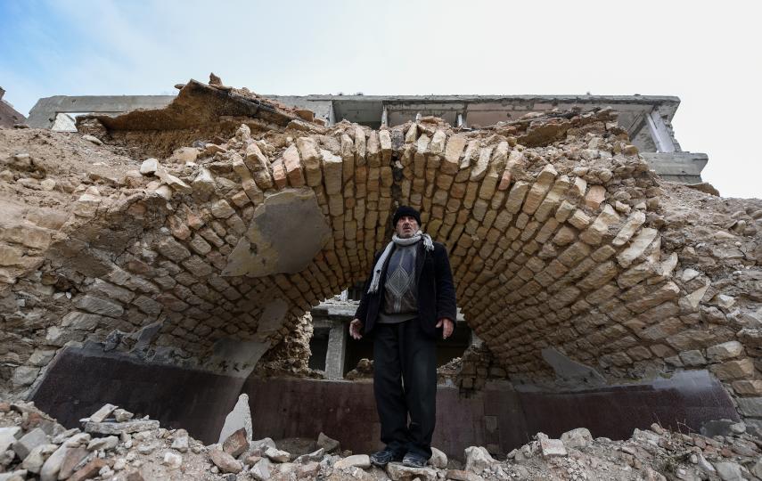 Badr el-Din Mouhanna stands under a brick arch of a building that has been turned into rubble.