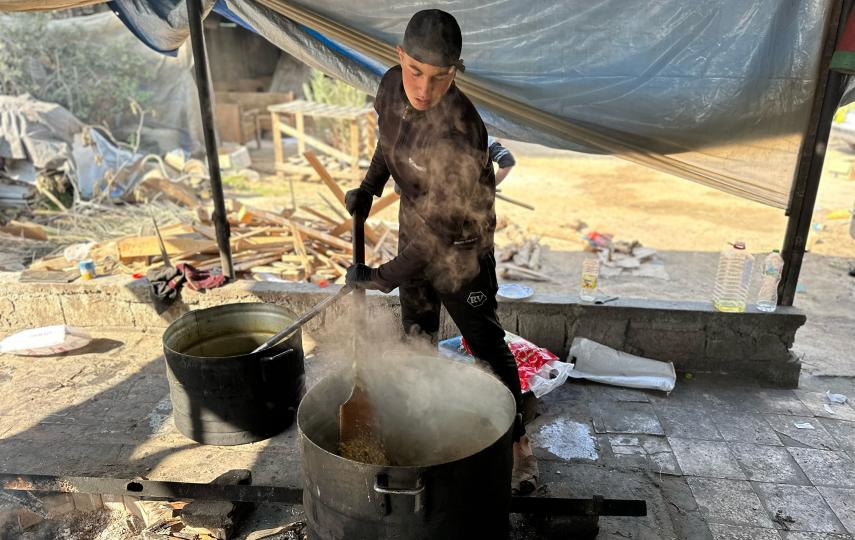 A person stirs food in a large pot at a community kitchen.