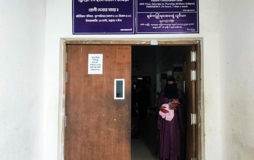 A woman holding a baby stands at the frame of a door at the Friendship Hospital Ukhiya in Myanmar