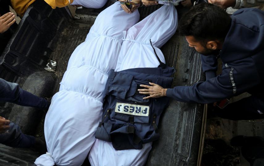 A photo of mourners as they gather around the bodies of two Palestinian journalists who were killed in Israeli strikes, amid the Israel-Hamas conflict. Their bodies are wrapped in white sheets and one has a press vest on it.